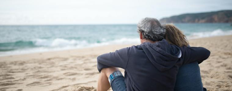 husband and wife sitting on beach with arms around each other