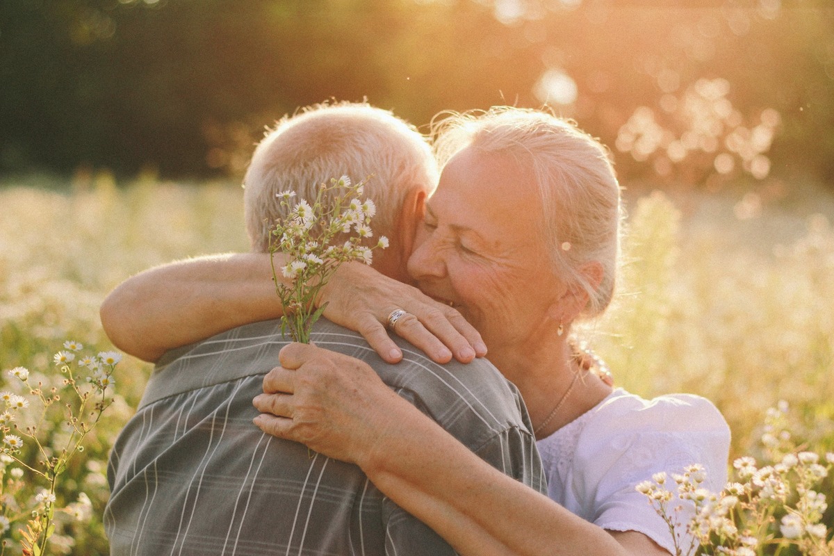 elderly woman hugging her husband among field of flowers