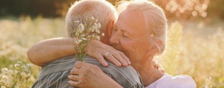 elderly woman hugging her husband among field of flowers