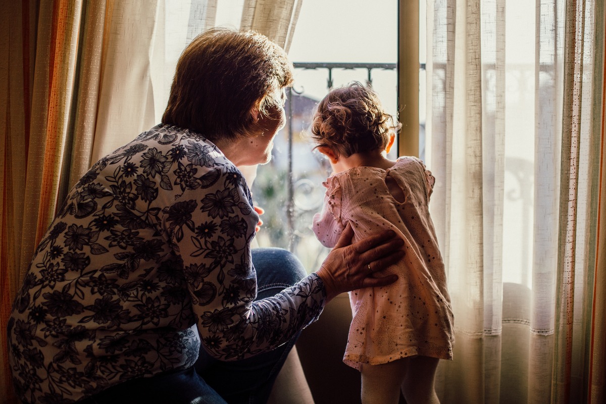 grandmother looking out a window with her arm around her granddaughter