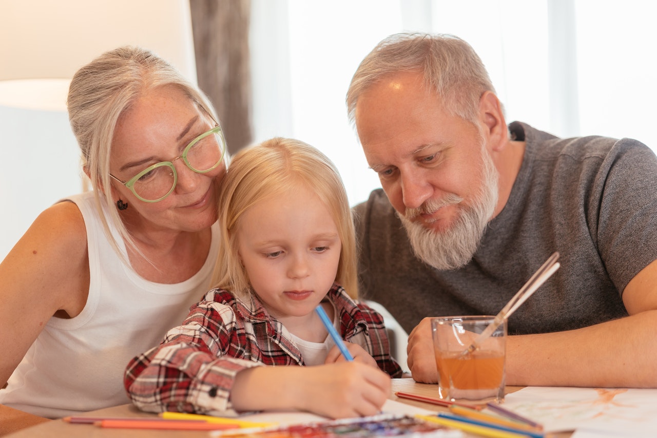 grandparents watching granddaughter color at table