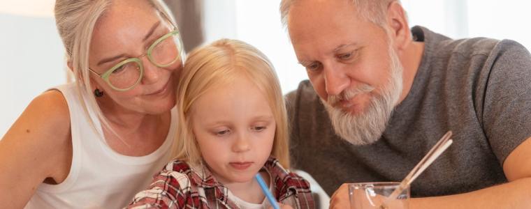 grandparents watching granddaughter color at table