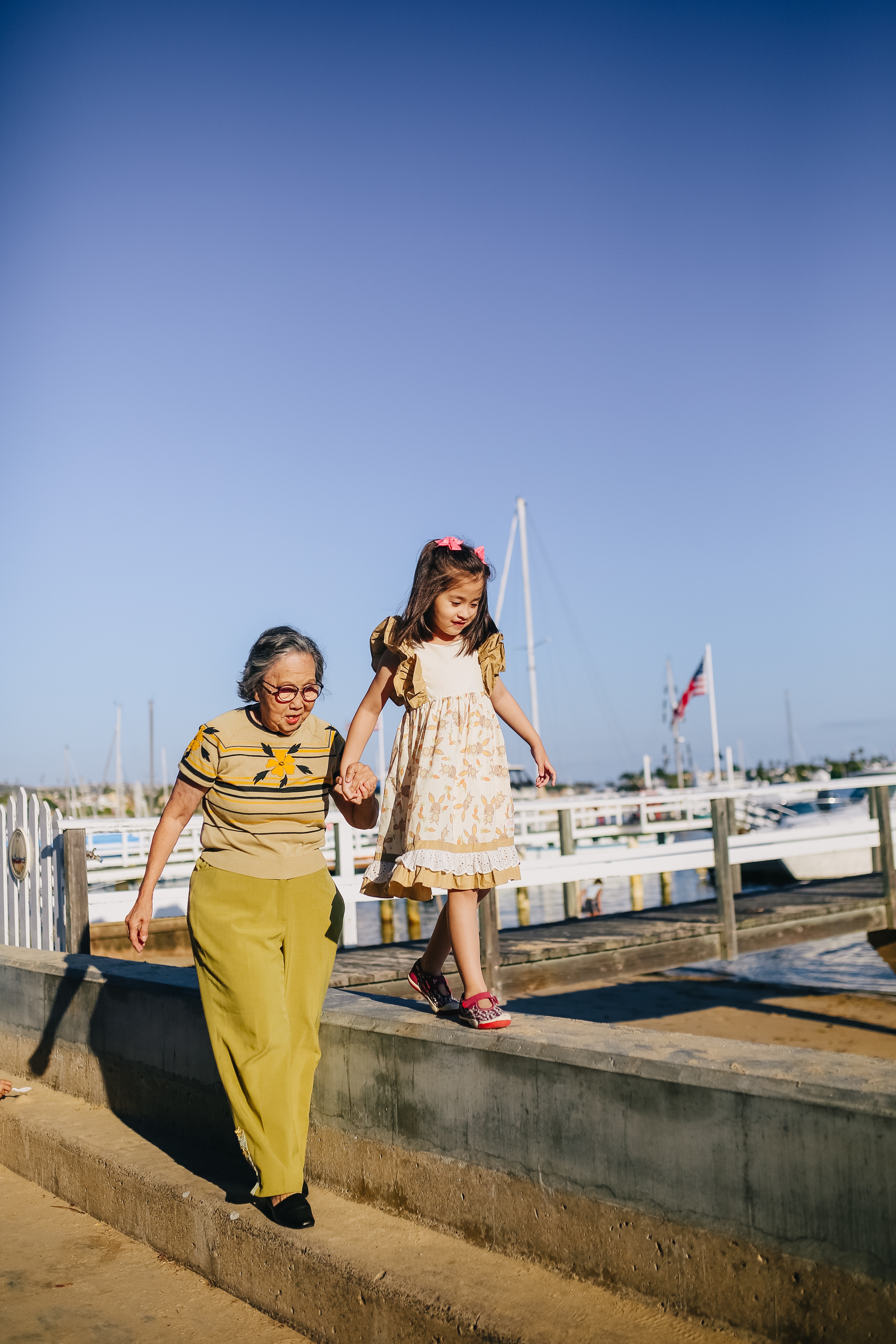 grandmother and granddaughter walking along water path next to boats