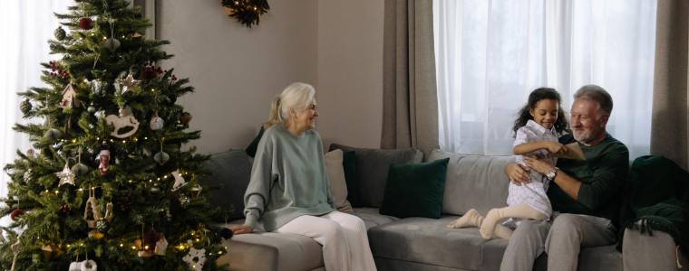 grandparents sitting with their granddaughter next to a Christmas tree